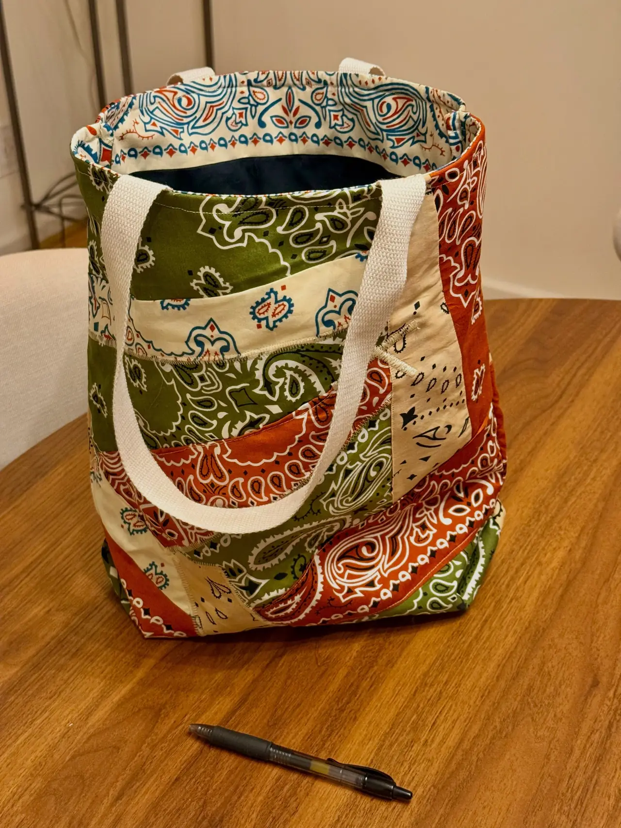A sewn tote made from green, rust, and cream bandana fabrics with pale woven handles