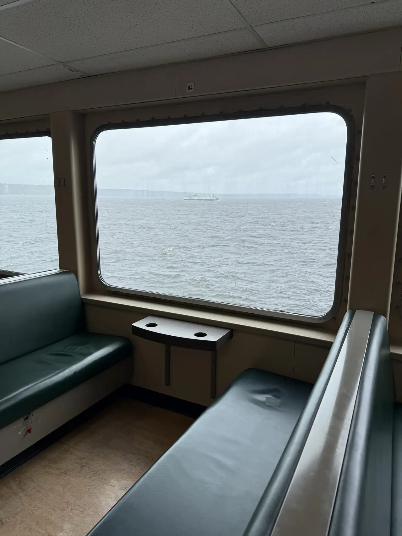 Teal seats beside a ferry window looking across the water toward another boat