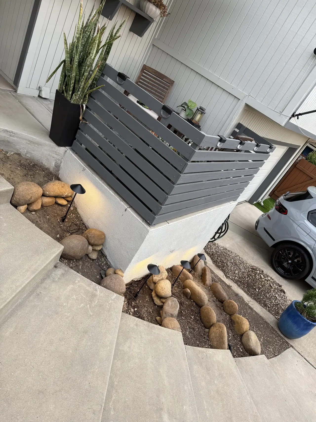Curved front steps beside a small bed of river stones and path lights, a fenced entry, and a driveway