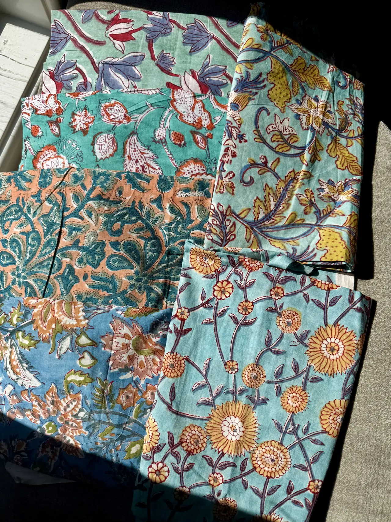 An assortment of turquoise, pale blue, and peach fabrics printed with flowers, leaves, and paisley motifs