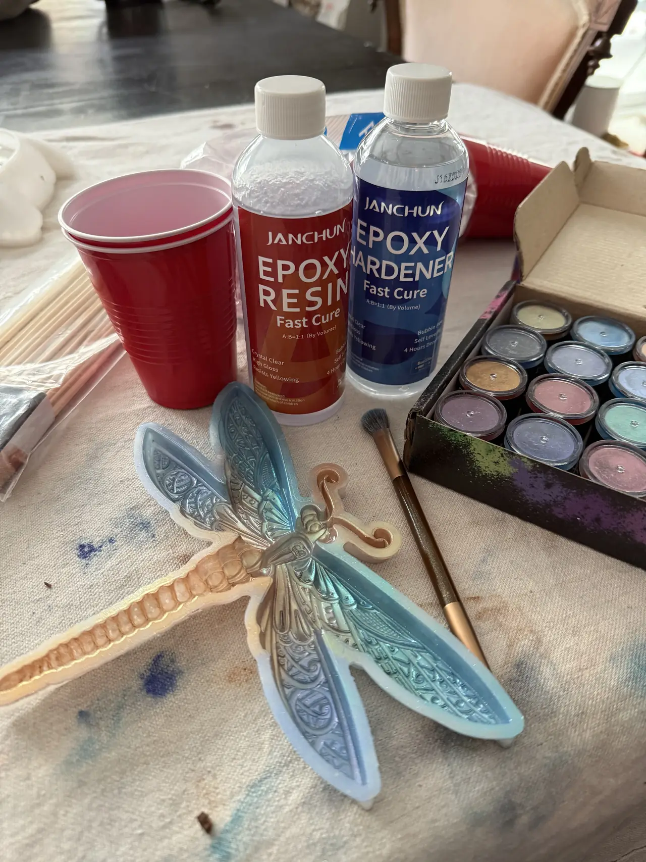 A resin craft project in progress with a dragonfly mold, pigments and a brush
