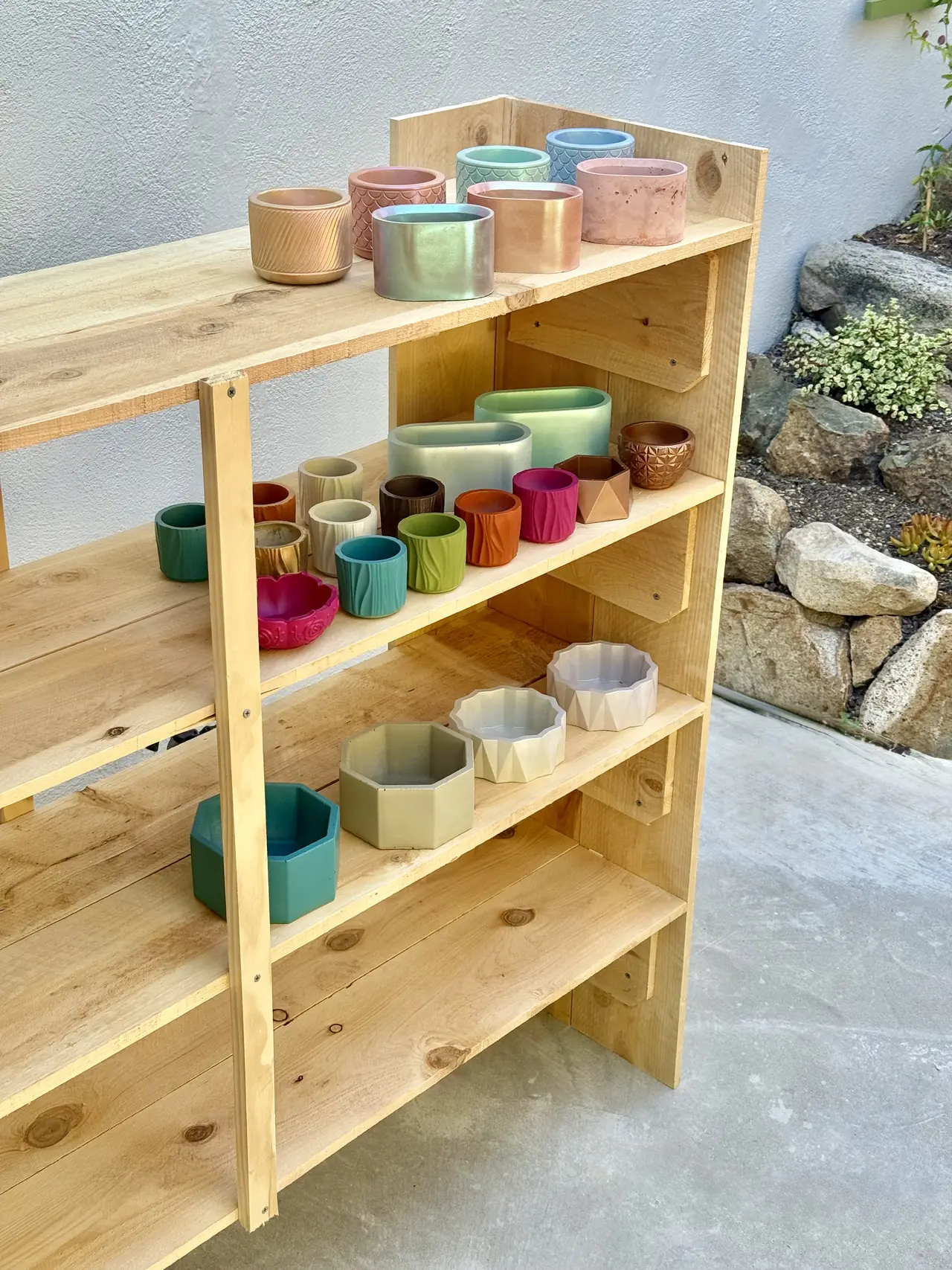 A wooden shelf of small handmade planters in soft colors