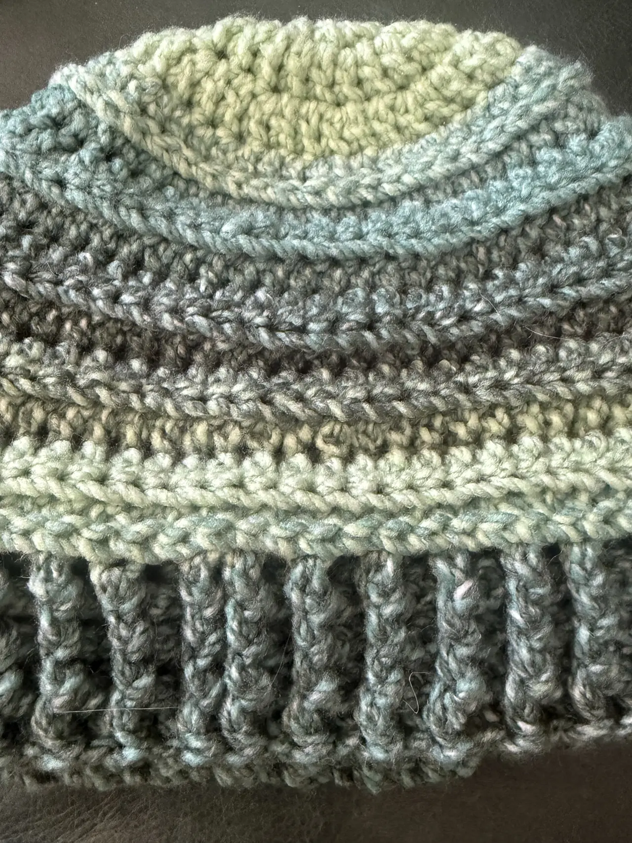 Close-up of crochet stitches on a hat in blue-green and gray yarn