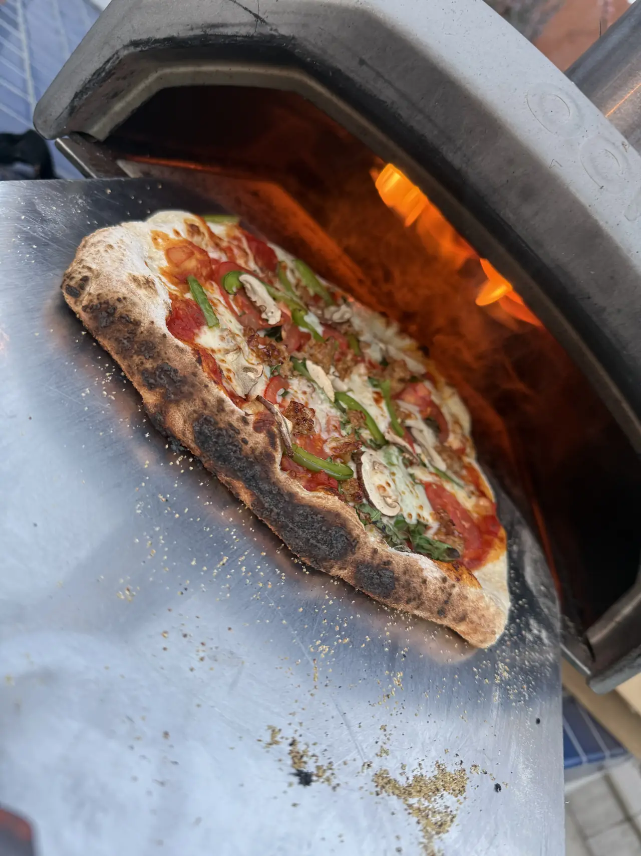 A homemade pizza coming out of a wood-fired pizza oven
