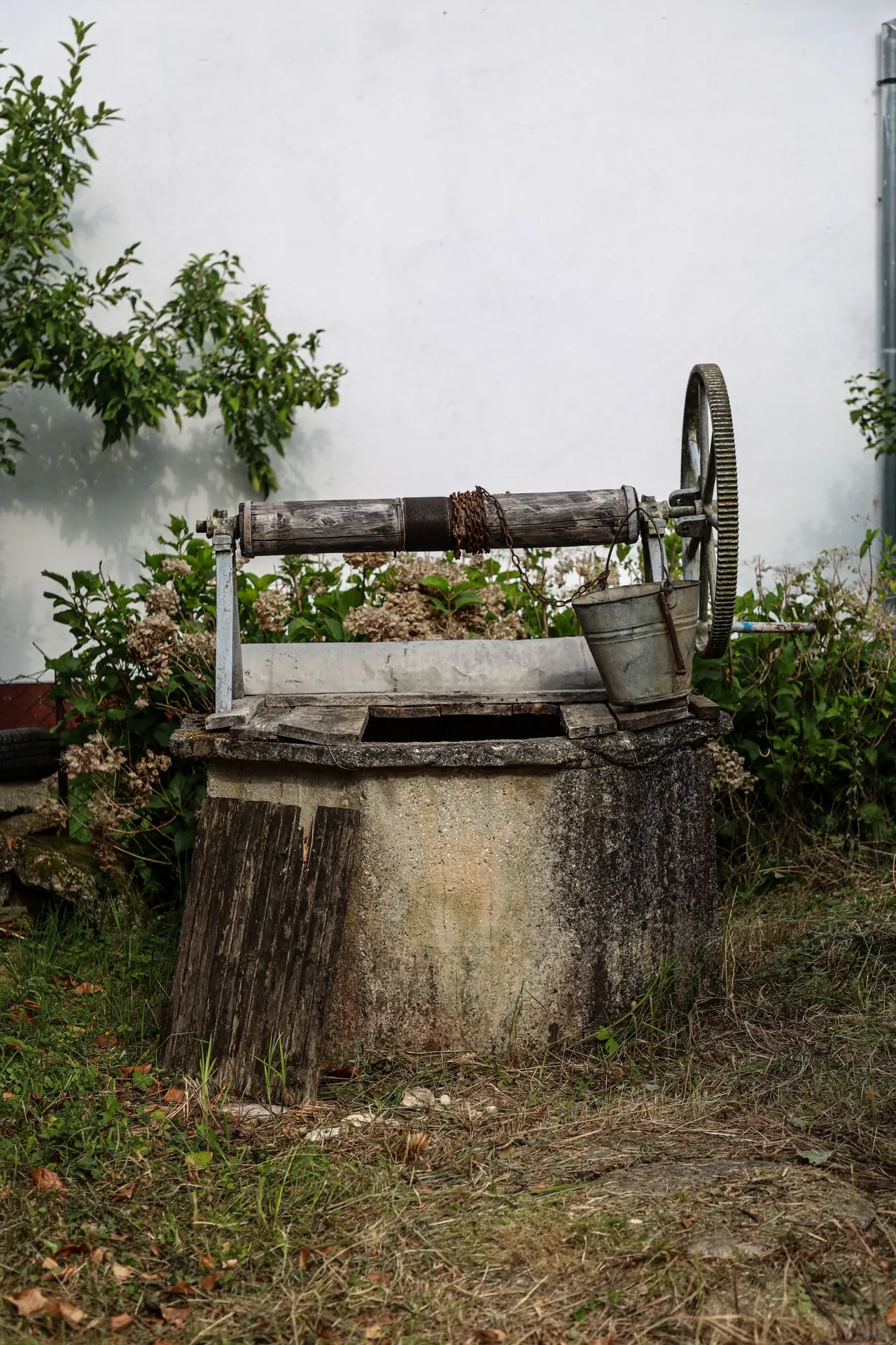 An old masonry well with a wooden spindle, metal wheel, chain, and bucket in a garden
