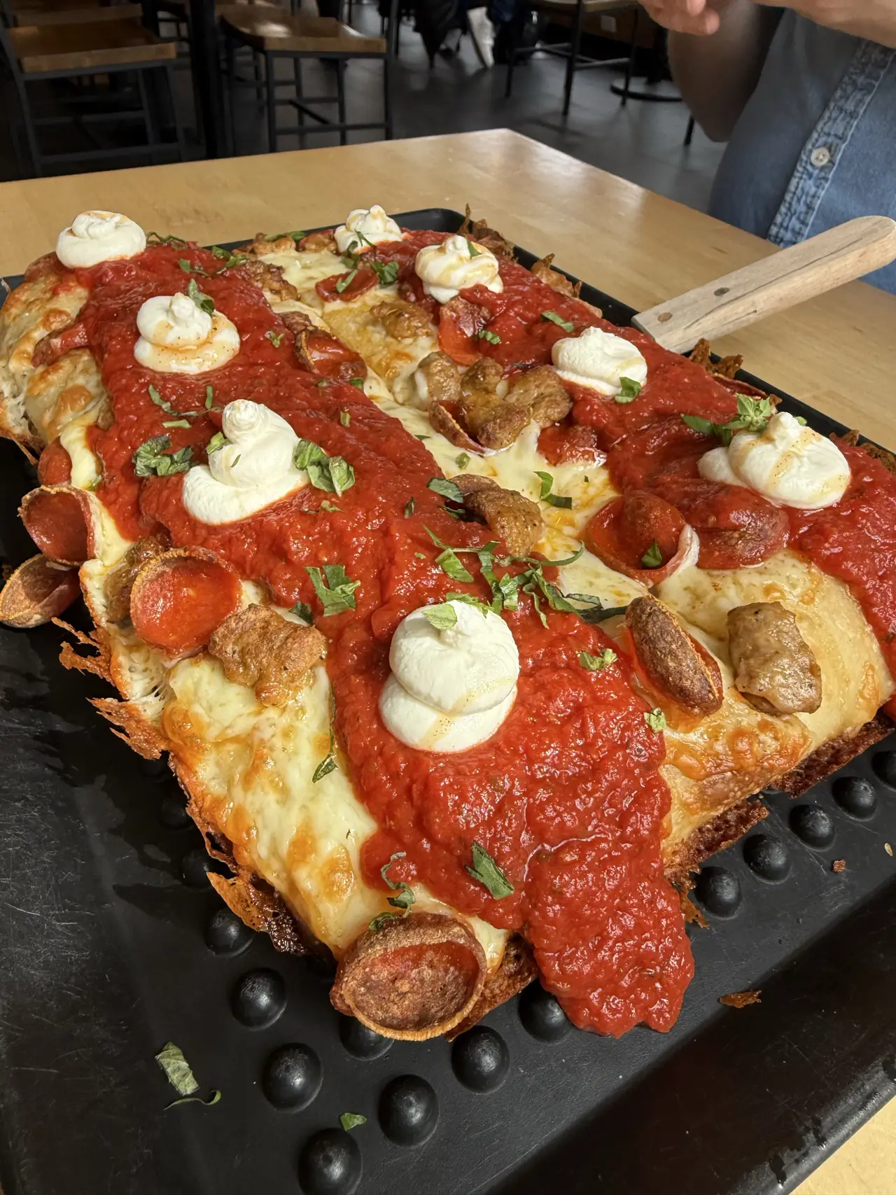 Square pizza with red sauce, cheese, and herbs on a black tray at Sourdough Willy’s